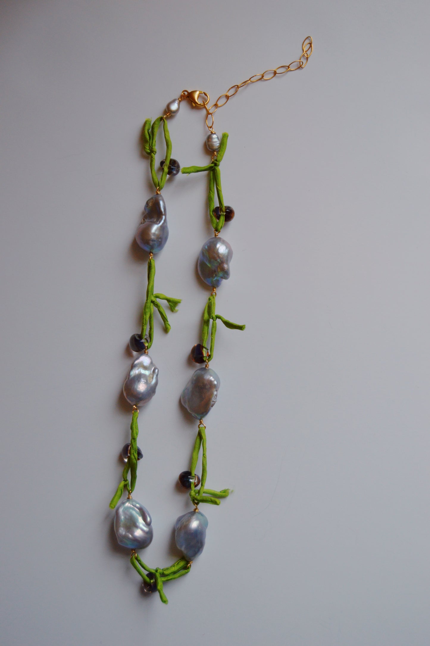 Silk and Pearl Layer- Tahitian Palm: A handmade necklace with irregular, shiny gray freshwater pearls and dark beads on a bright green knotted cord, finished with a gold clasp and extension chain, displayed on a white background.