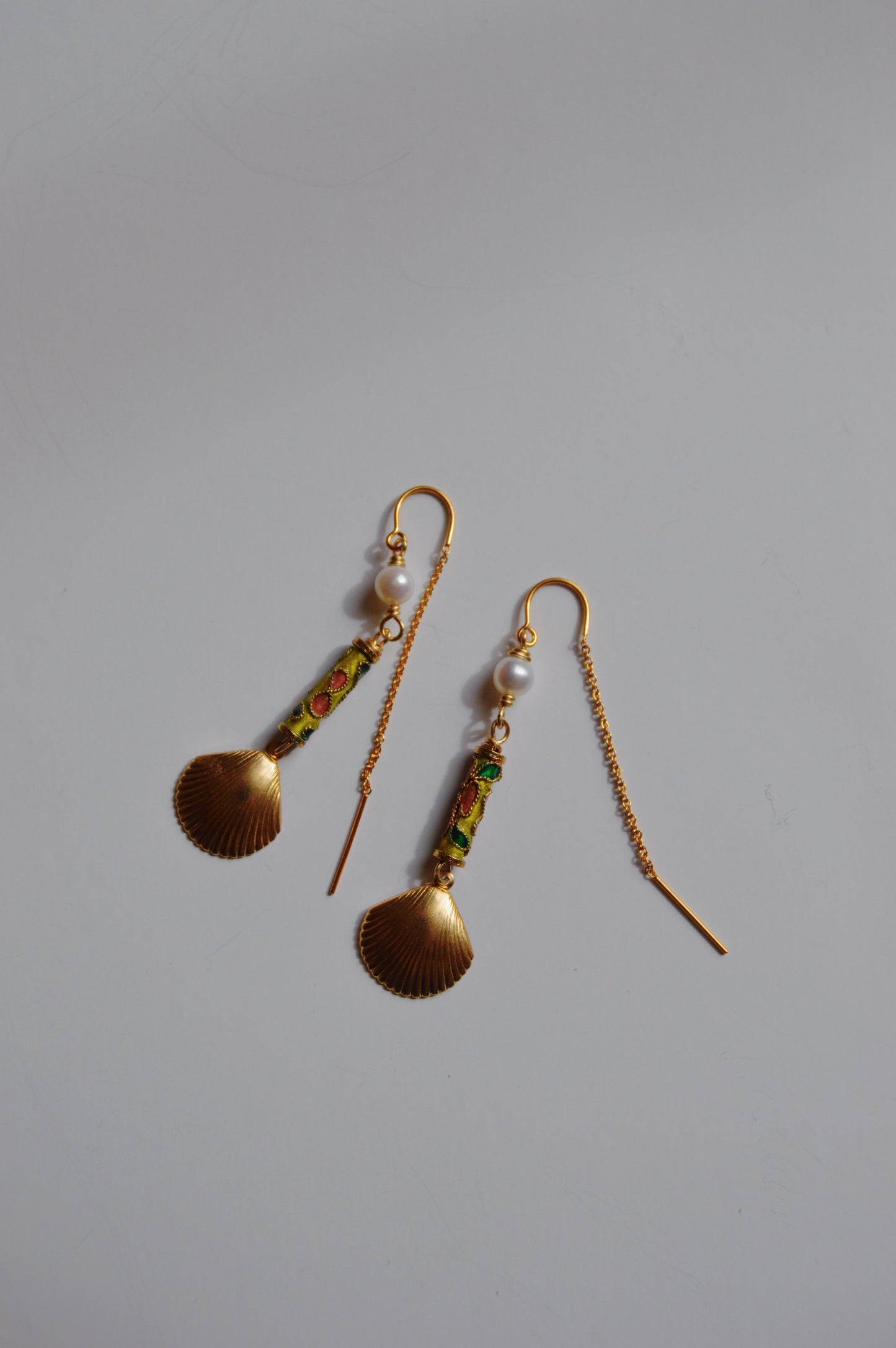 The Cloisonne Shell Threaders are gold drop earrings featuring scallop shell-shaped pendants, cultured freshwater pearls, and green and red detailing—handcrafted artisan jewelry that shines on a plain white background.