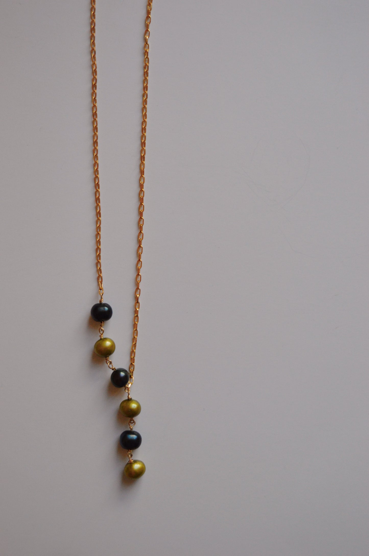 The Six Pearl Lariat—Blue and Green Mix is a handcrafted necklace featuring six alternating blue and green pearls in a vertical line on a 14k gold-filled chain, showcased against a plain light background.