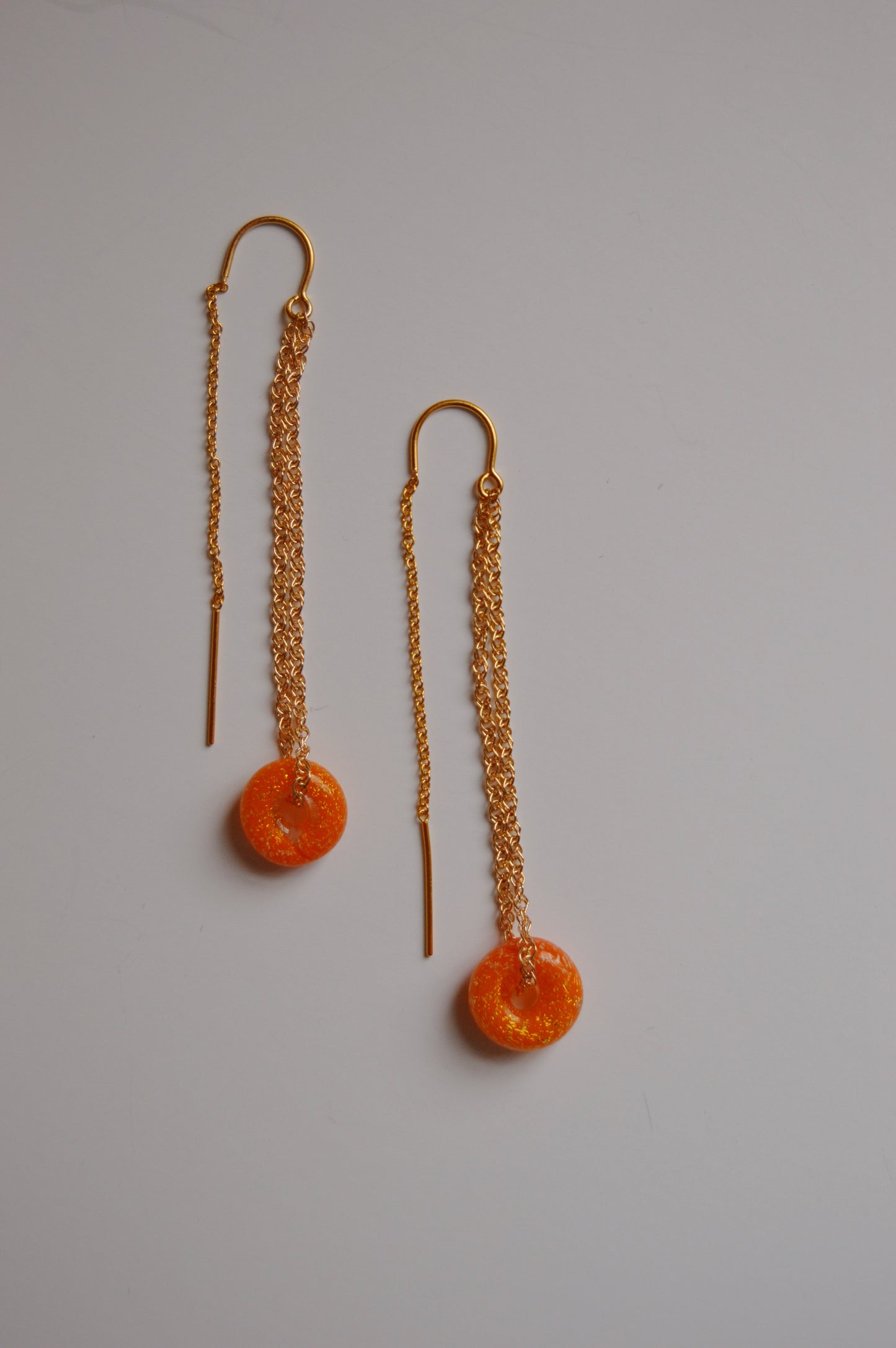 A pair of Donut Threaders- Sunshine Sparkle earrings featuring gold chains, orange handmade lampwork glass beads, and straight gold bars, displayed on a plain white background.
