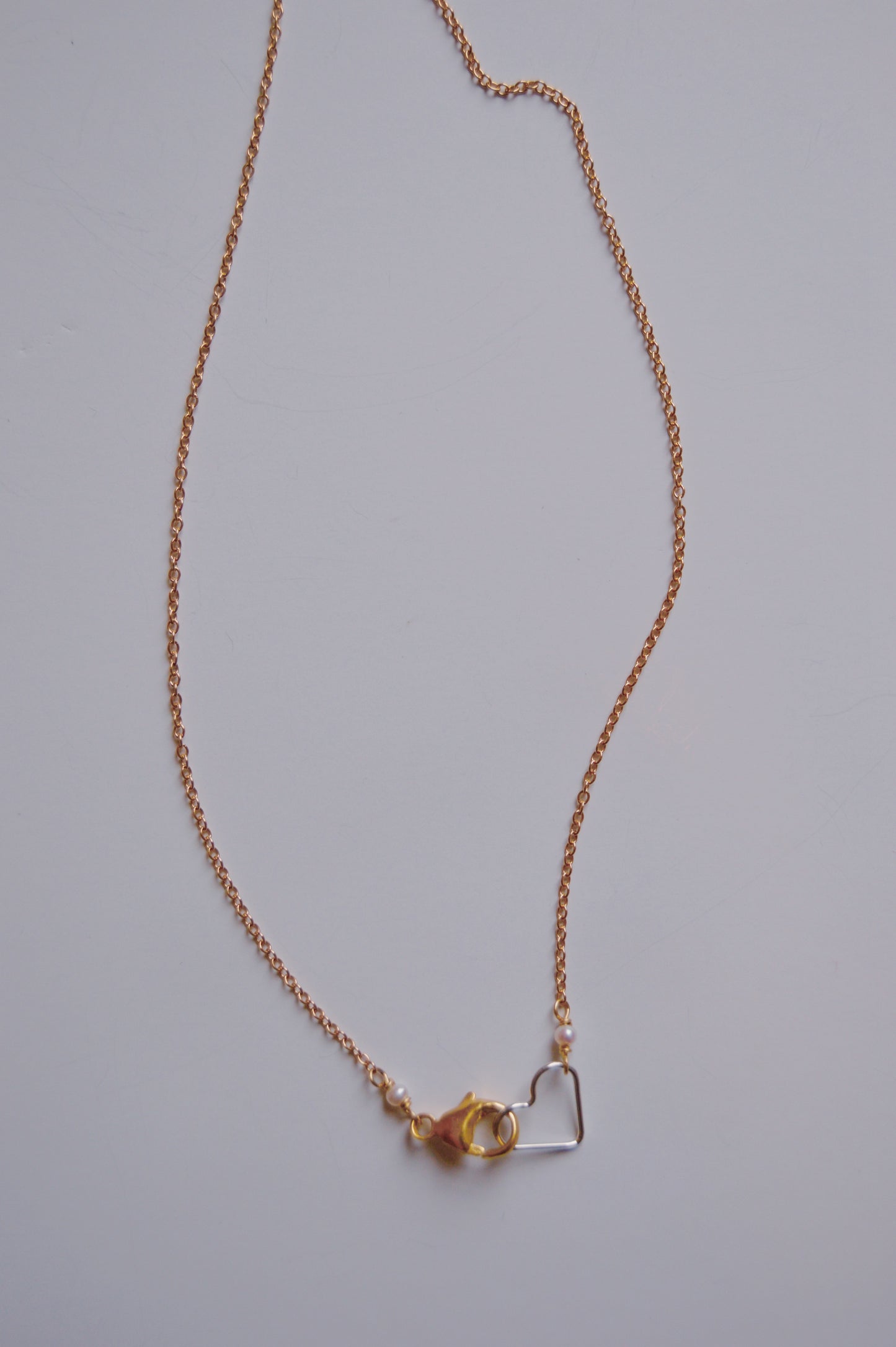 The Clasp in Front Layer necklace features a delicate 16" oxidized sterling silver chain with a lobster clasp and a small 14K gold-filled heart pendant, shown against a plain white background.