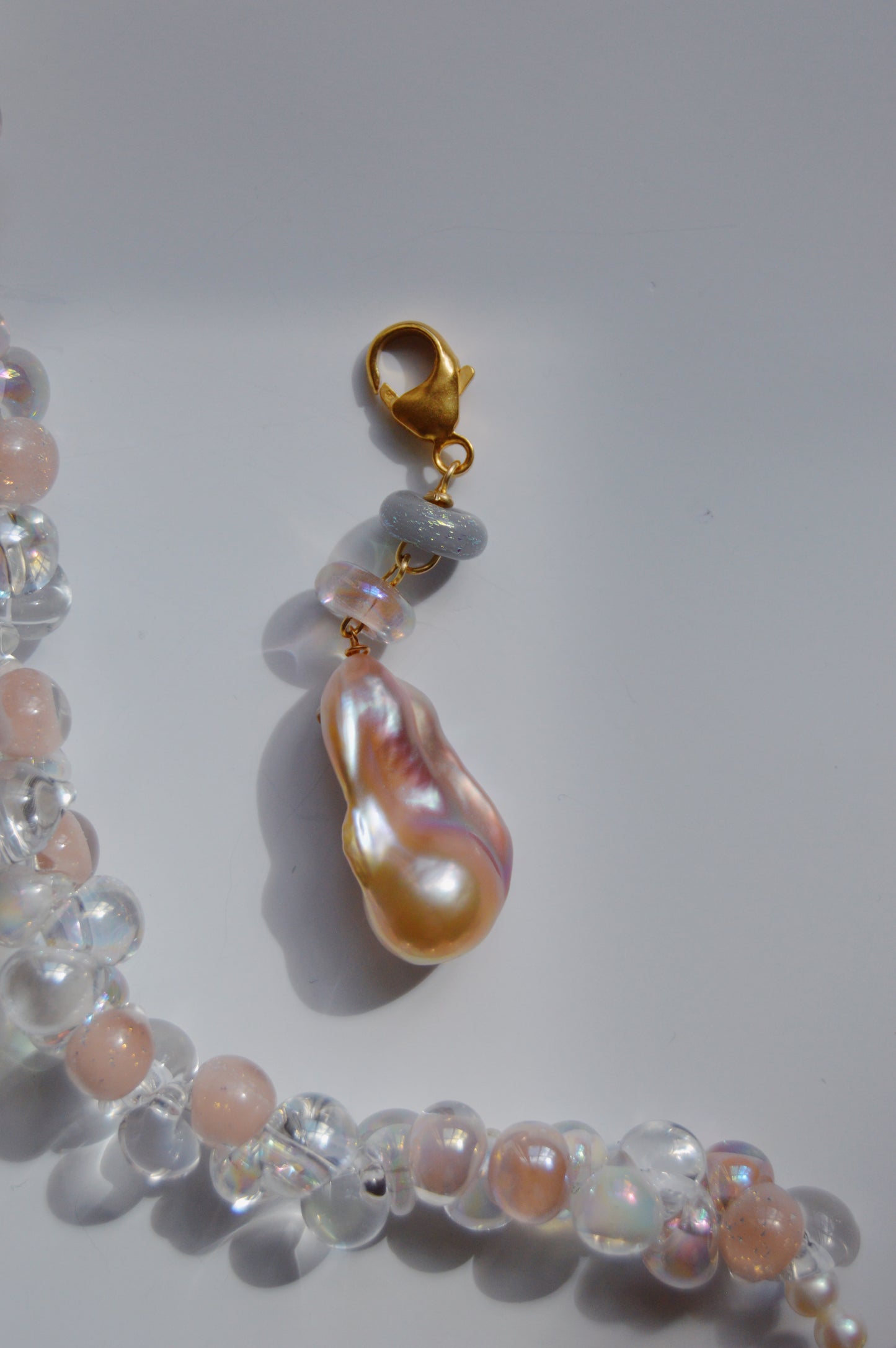 A close-up of the Glass and Pearl Charm necklace with clear and peach handmade lampwork glass beads, 14k gold-filled findings, and a large baroque freshwater pearl charm, displayed on a white background.