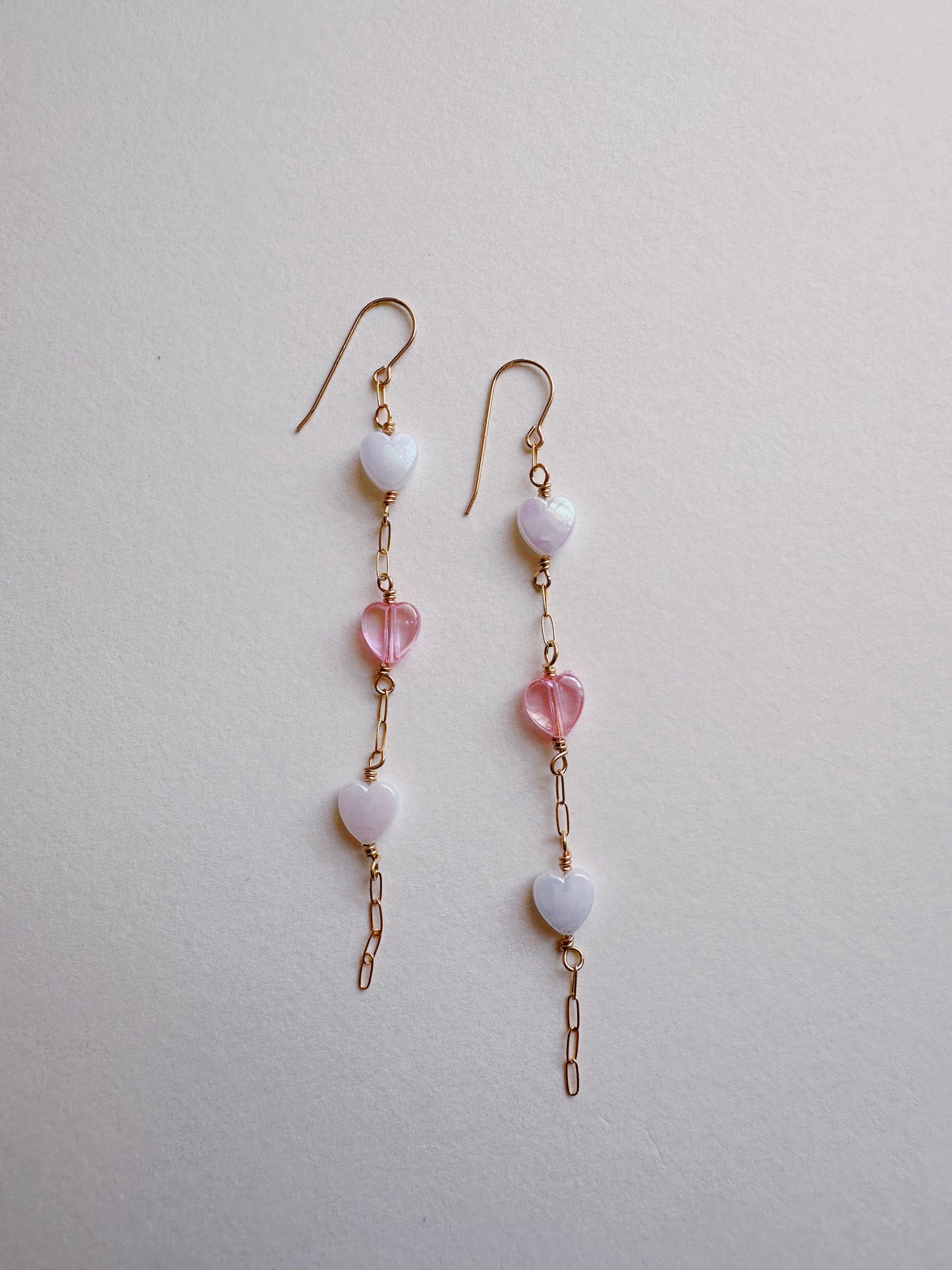 Acrylic Heart Drops: Delicate dangle earrings with gold filled hooks and chain, each showcasing two white and one pink acrylic hearts, displayed on a light background.