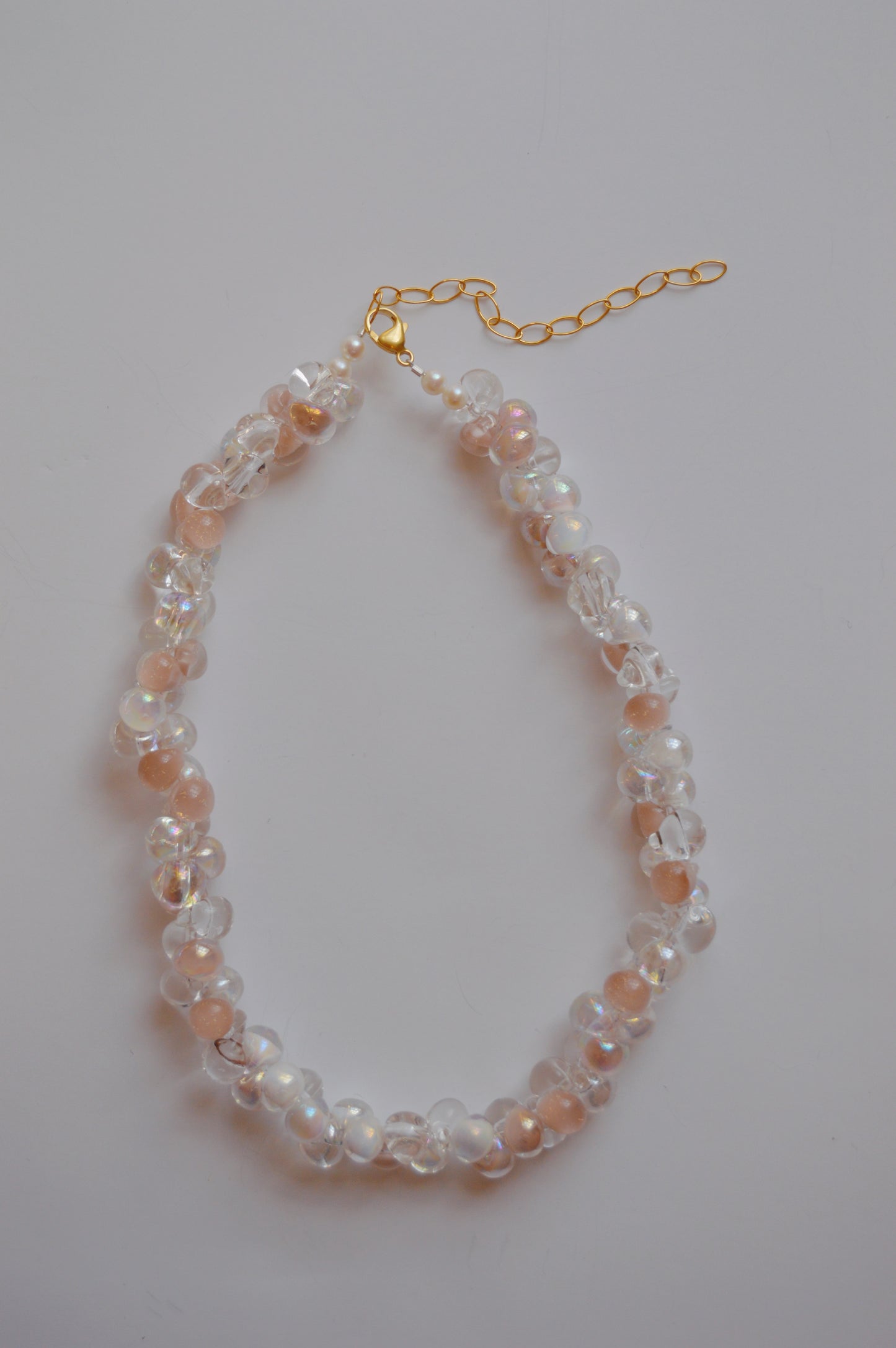 The Bubble Glass Necklace- Neutral Mix is a handmade necklace with alternating clear and peach glass beads, finished with a gold chain extender and clasp, shown on a plain white background.