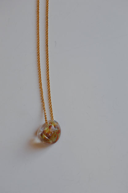 The Grand Bubble Single - Mars is a 14k gold filled chain necklace featuring a clear, irregularly shaped glass pendant with orange and yellow accents, shown against a plain white background.