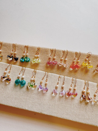 Bubble Minis: Colorful glass bead earrings with gold-filled findings, displayed neatly in rows on a beige fabric board. Available in green, blue, pink, yellow, and purple.
