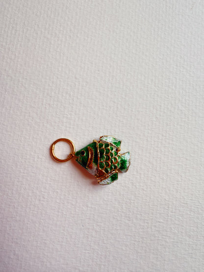 The Fish Anklet features a small green cloisonné fish charm with gold accents and a gold loop, displayed on textured white paper.