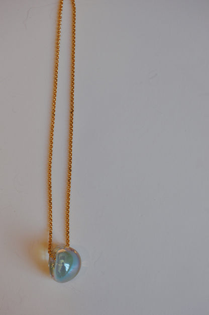The Grand Bubble Single - Shimmer Blue features a 14k gold filled chain necklace with a shimmering blue, heart-shaped pendant displayed on a plain white background.