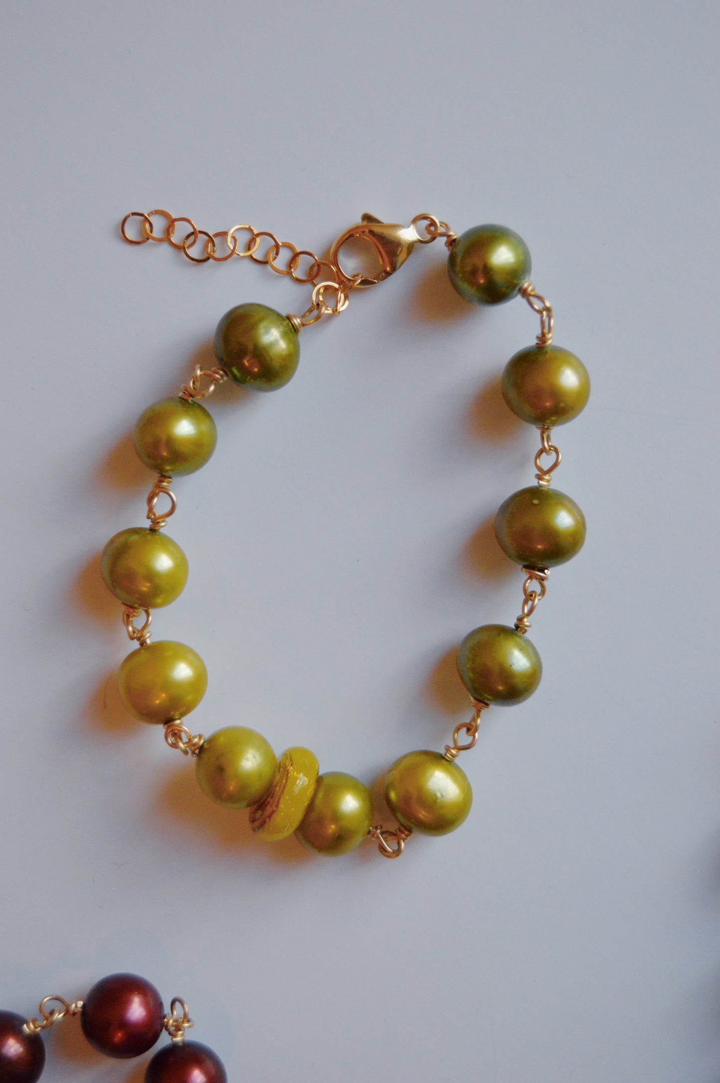 The Pearl and Glass Bracelet in green features handmade lampwork glass beads on a 14k gold-filled chain with a lobster clasp, displayed on a white background.