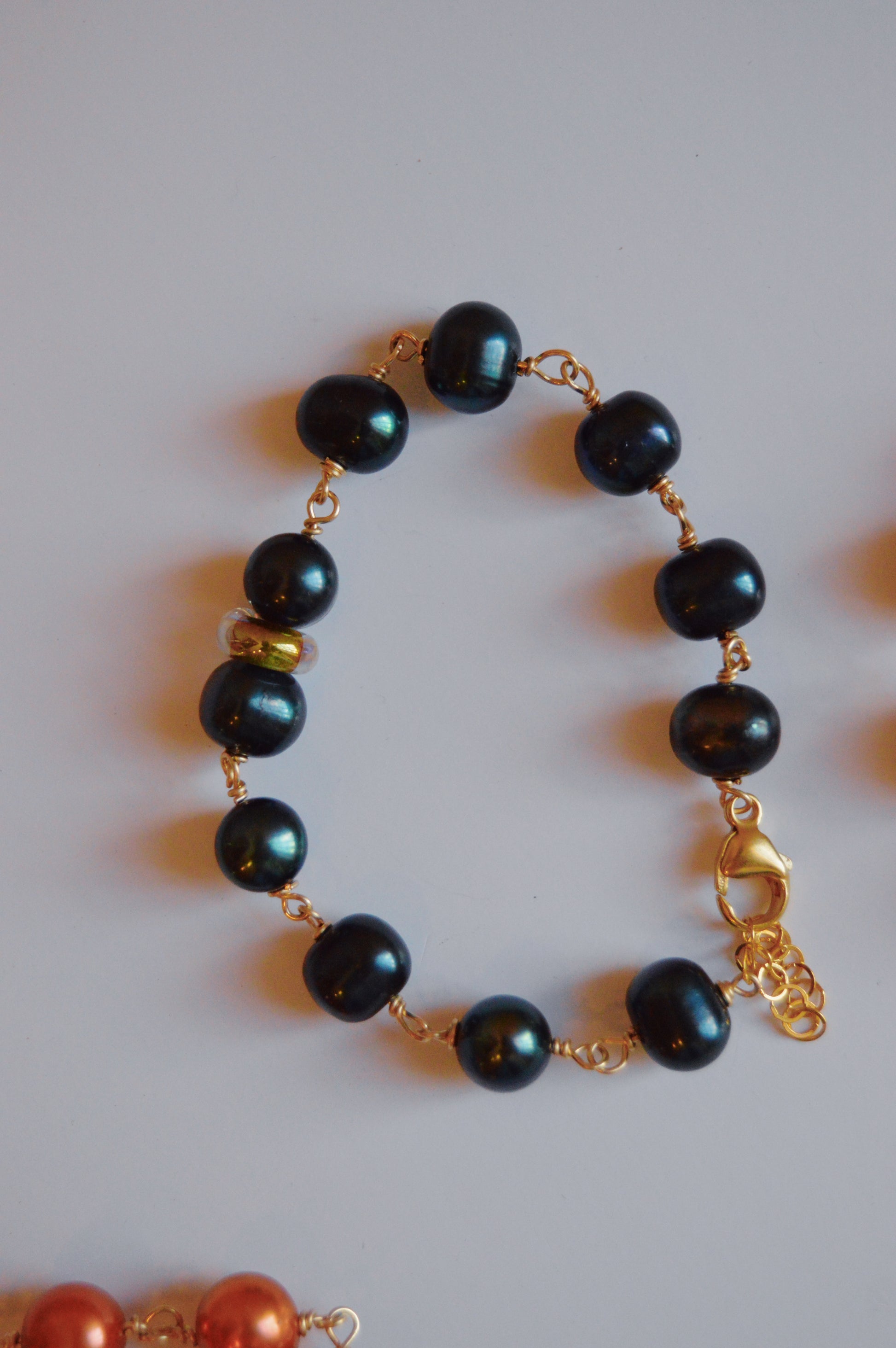 The Pearl and Glass Bracelet features dark teal round beads, including handmade lampwork glass, linked with a 14k gold-filled chain, a single gold bead, a gold clasp, and an extension chain, shown on a white background.