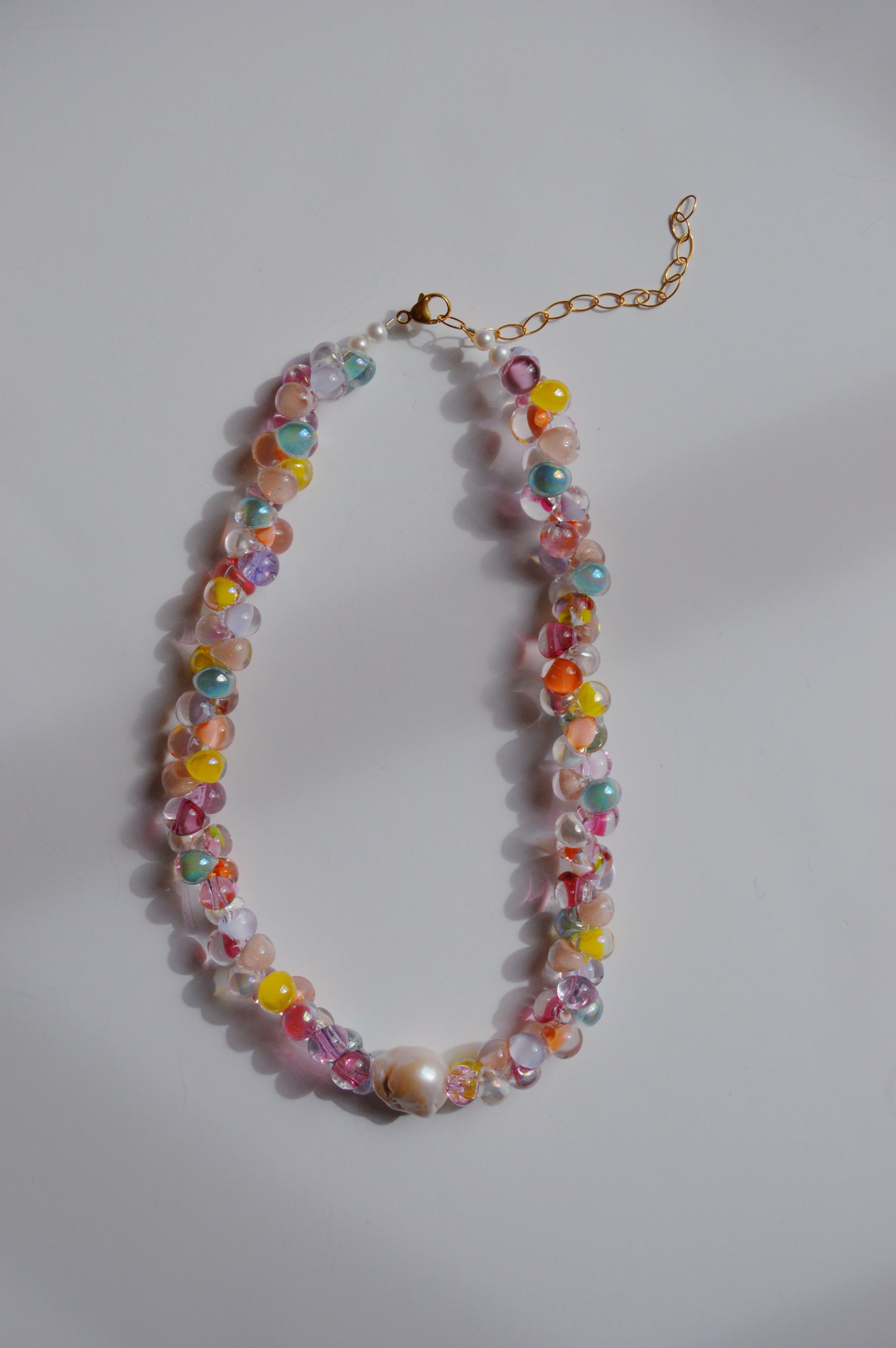 The Rainbow Bubble Glass Necklace in hop color features two strands of assorted beads with a large cultured freshwater pearl at the center and a gold chain clasp, displayed on a white background.