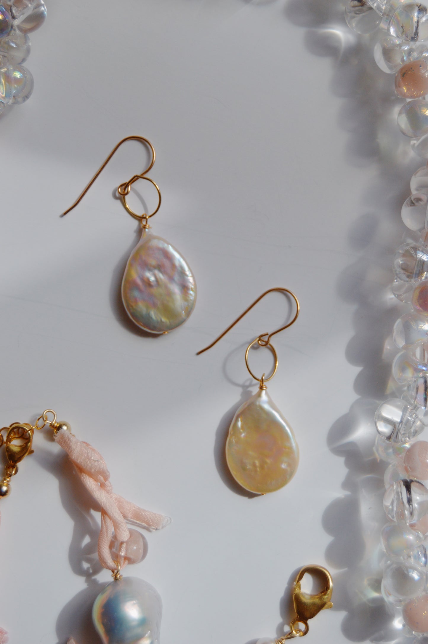 Pearl Drops: 14k gold-filled hook earrings featuring iridescent cultured freshwater pearl pendants, accented with translucent beads and light pink fabric, displayed on a white background.