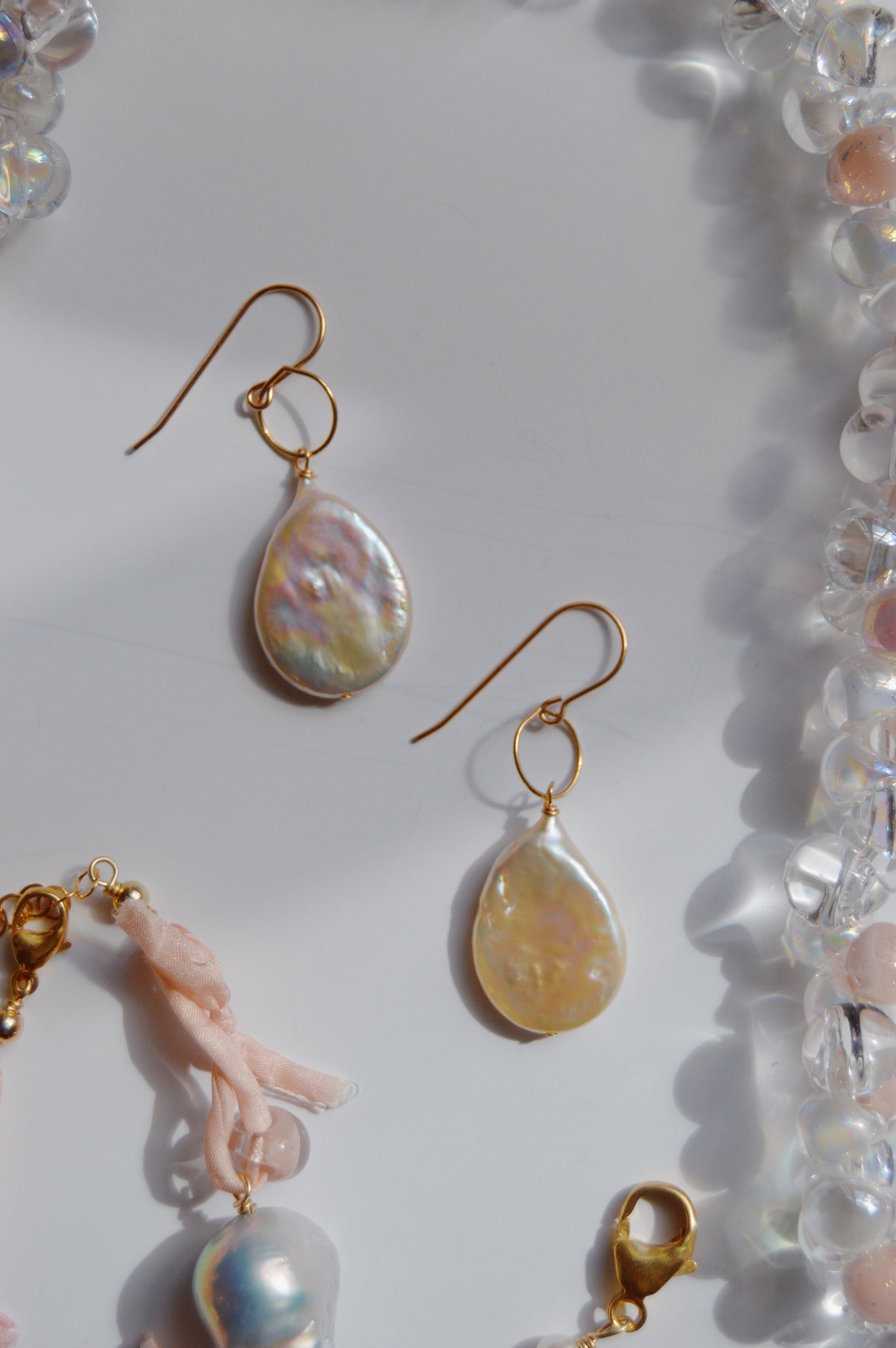 Pearl Drops: 14k gold-filled hook earrings featuring iridescent cultured freshwater pearl pendants, accented with translucent beads and light pink fabric, displayed on a white background.