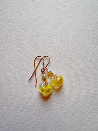 Bubble Minis are gold hook earrings with gold filled findings, small white beads, and translucent yellow donut-shaped charms, shown on a textured white surface.
