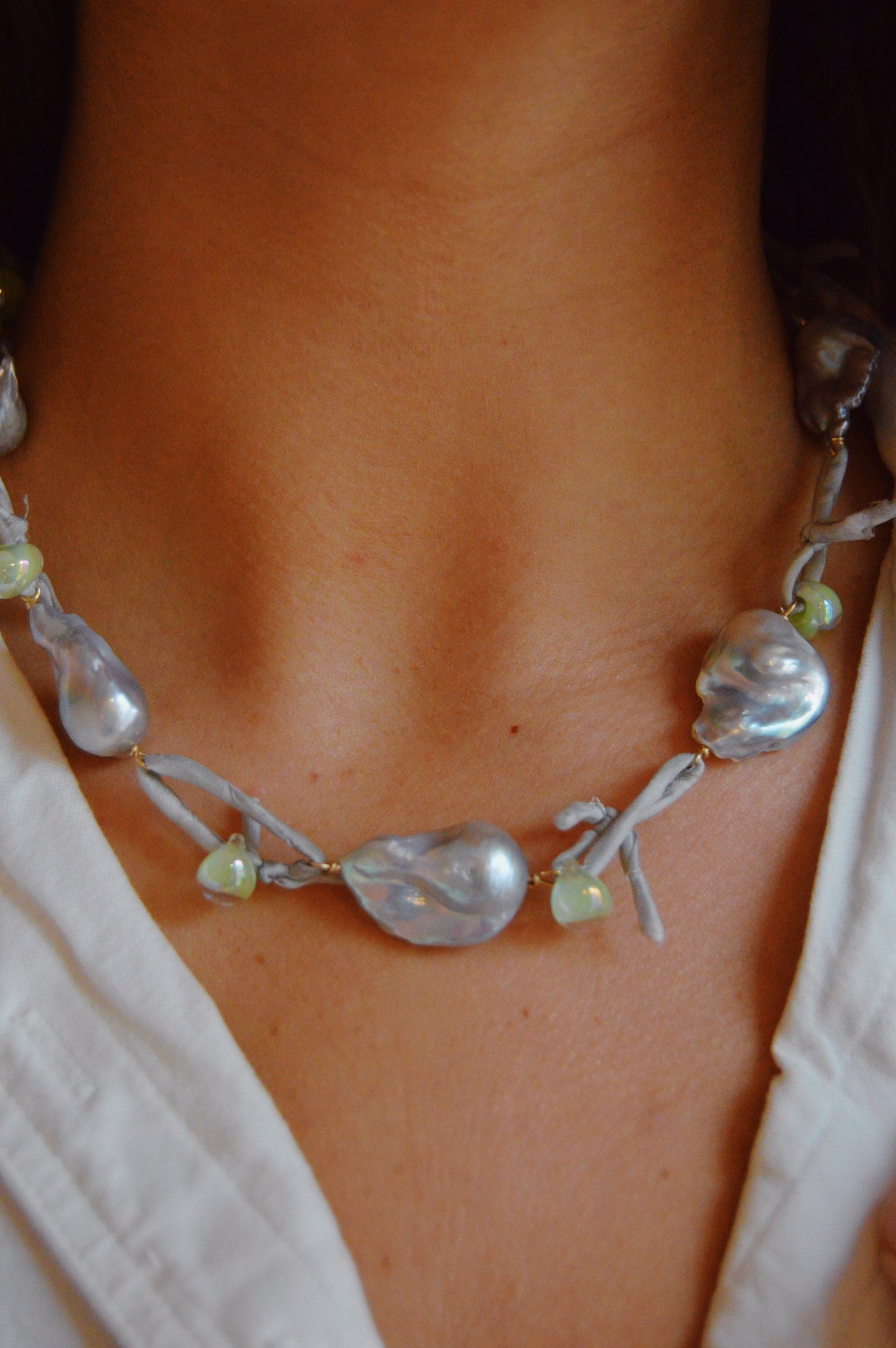 A person in a white shirt showcases the Silk and Pearl Layer- Silver Shores necklace, handmade with large, irregular silver pearls and light green beads for a unique freshwater pearl look.