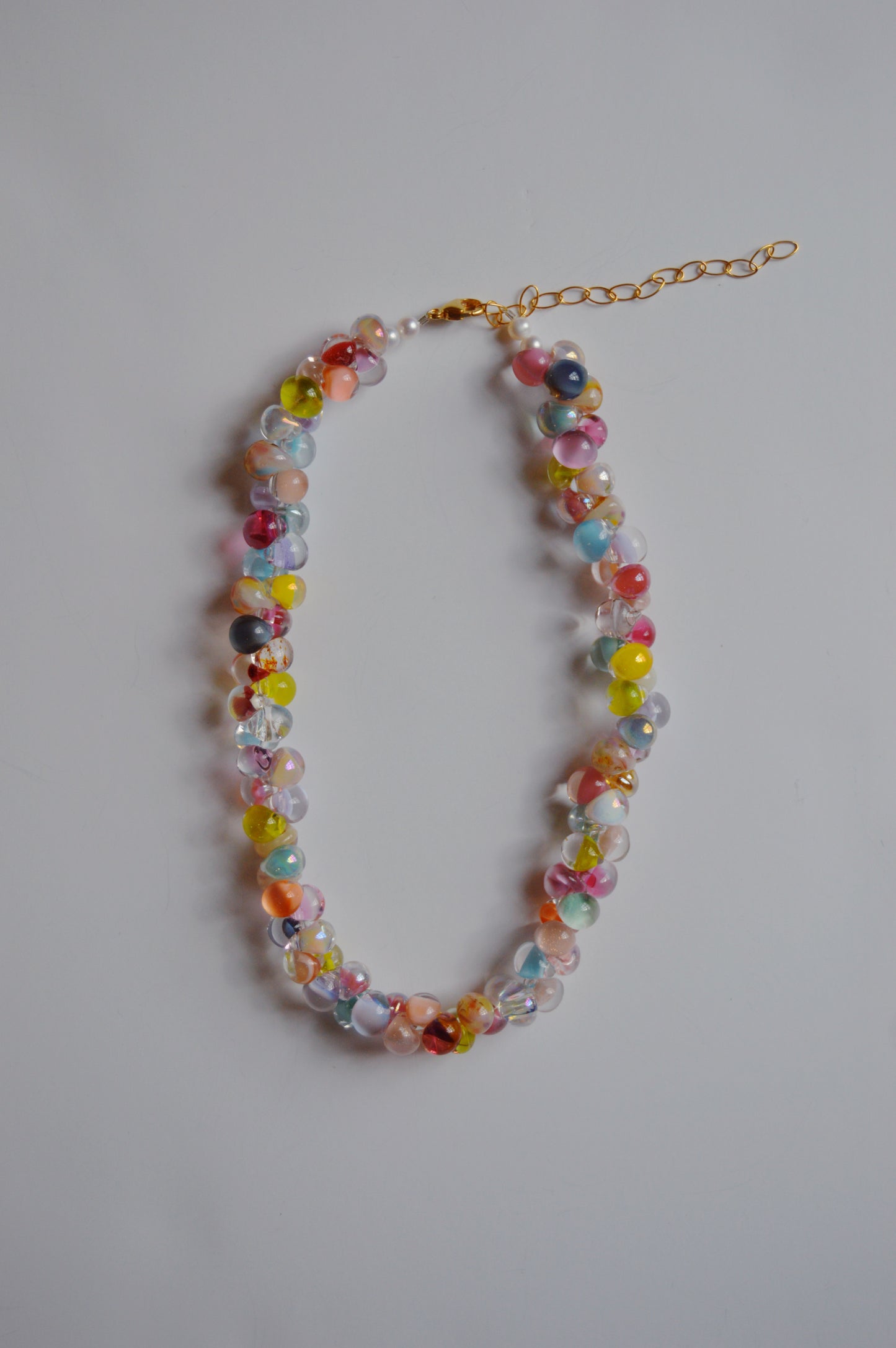 The Rainbow Bubble Glass Necklace features handmade lampwork glass beads in a vibrant jellybean color palette and includes a gold chain extender, showcased on a plain light surface.