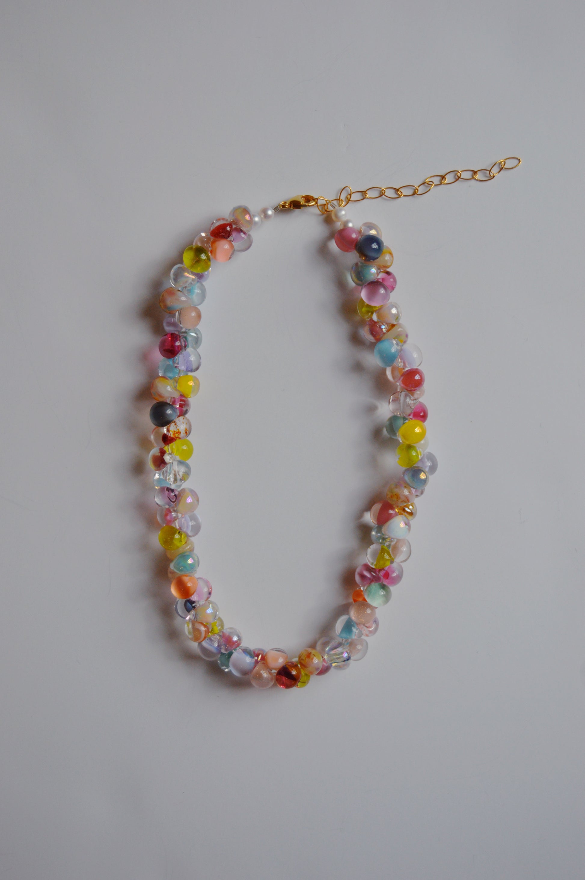 The Rainbow Bubble Glass Necklace features handmade lampwork glass beads in a vibrant jellybean color palette and includes a gold chain extender, showcased on a plain light surface.