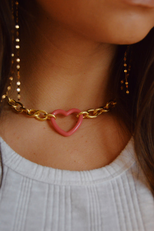 A close-up of someone wearing the Open Heart on Chunky Plated Chain, featuring a gold-plated chain and an open heart charm. They are dressed in a white, pleated top with their hair loosely framing their face.