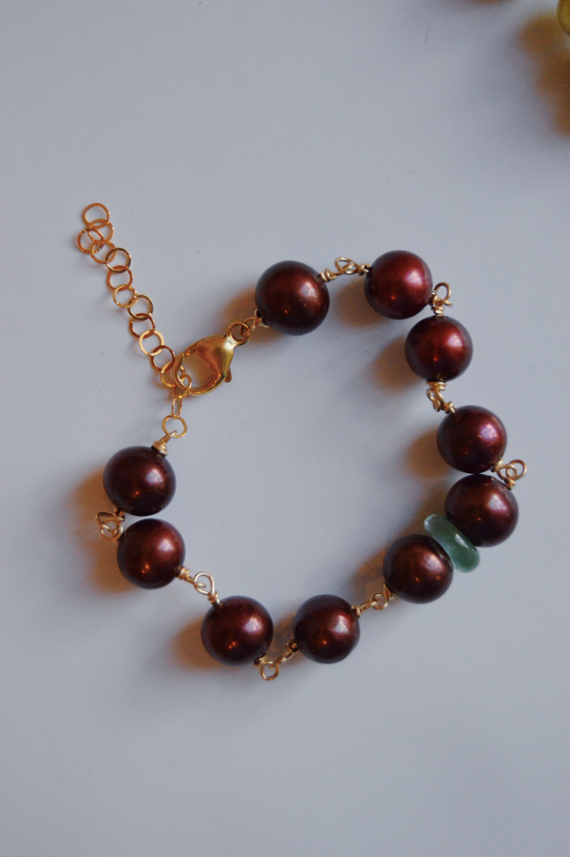 The Pearl and Glass Bracelet features large, round, purple beads and handmade lampwork glass beads, finished with a 14k gold-filled chain clasp. Displayed on a light gray surface.
