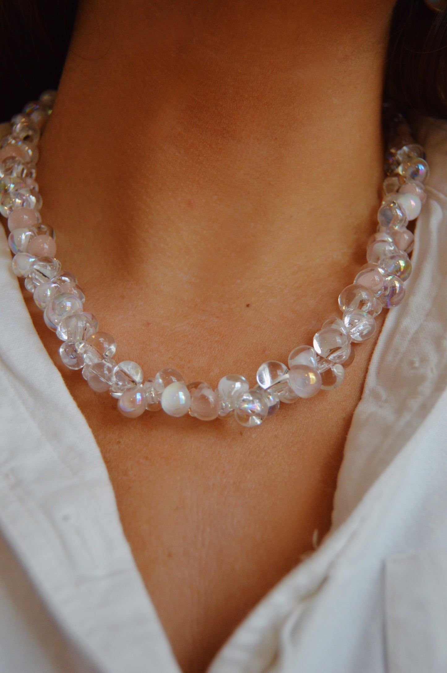 A close-up of a person wearing the Bubble Glass Necklace- Neutral Mix, a double-stranded handmade piece with clear and opalescent beads, styled over a white collared shirt.