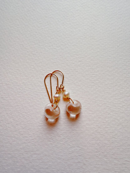Bubble Minis: Delicate gold wire earrings with freshwater pearls and clear glass beads, elegantly arranged on a textured white background.