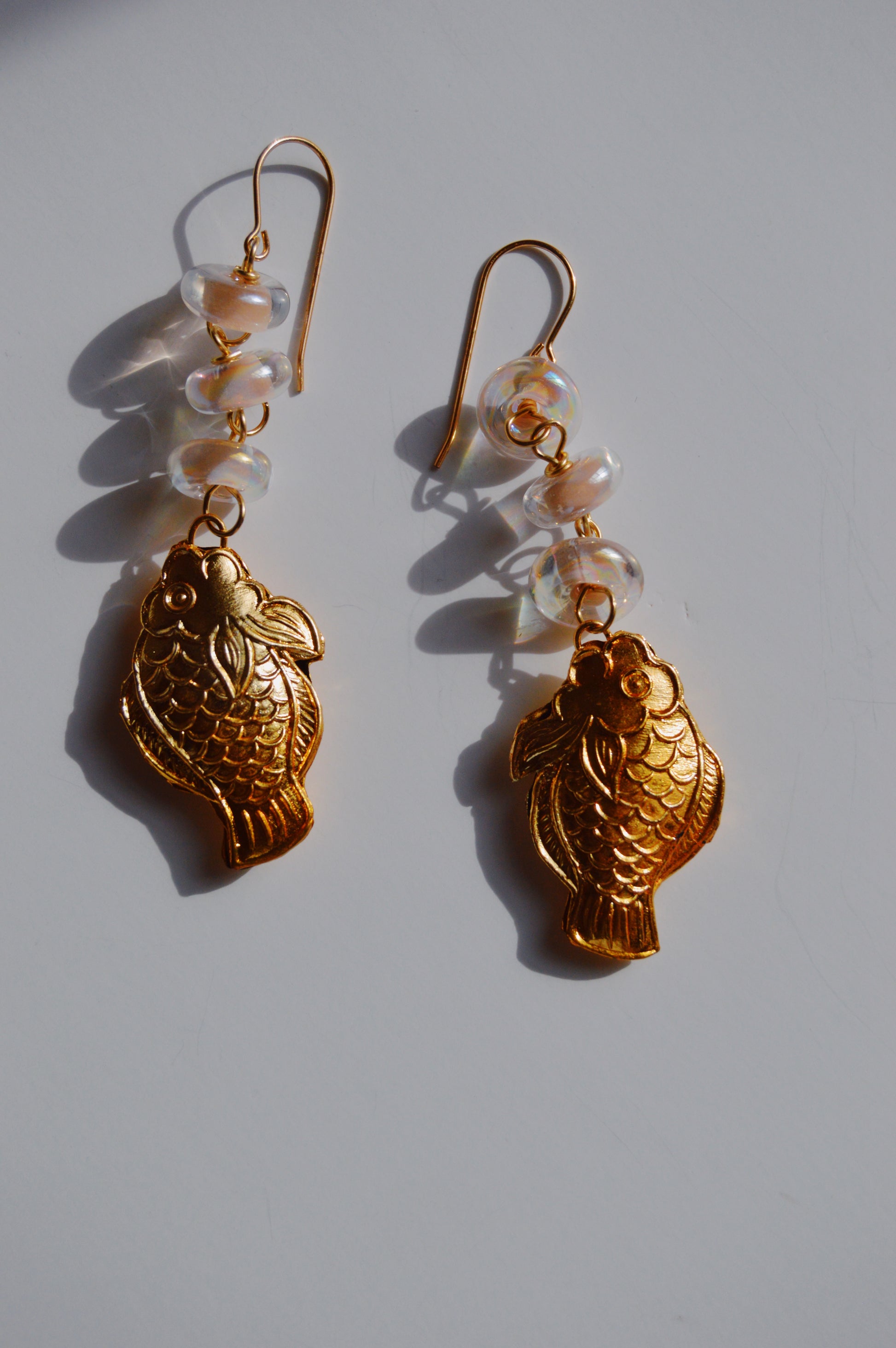 Fish and Glass Drops: Gold cloisonné fish charm earrings, each featuring three handmade lampwork glass beads above the fish, displayed on a white surface.