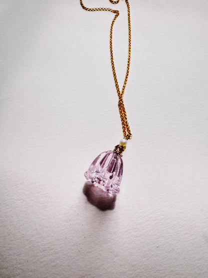 The Tulip Necklace features a 14k gold filled chain with a pendant shaped like a light purple handblown glass tulip bell, casting a delicate shadow on a white surface.