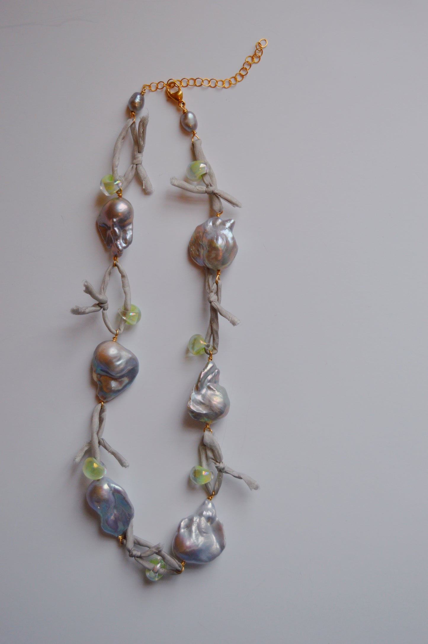 The Silk and Pearl Layer- Silver Shores is a handmade necklace with large, irregular silver freshwater pearls and small light green beads on knotted silk, finished with a gold chain extender and shown on a white background.