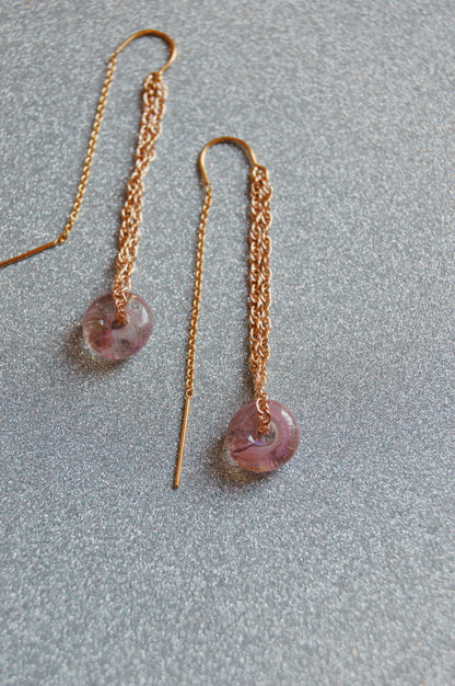 The Glass Donut Threaders feature round, translucent purple handblown glass beads on elegant 14k gold filled chain, displayed against a sparkling silver background.