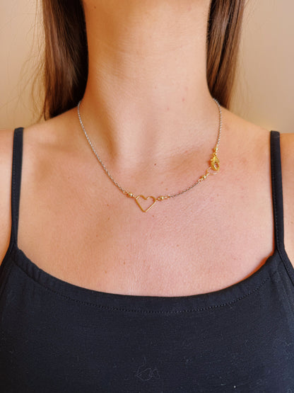 A woman wears the Clasp in Front Layer necklace: a 16-inch oxidized sterling silver chain with a 14K gold-filled heart-shaped pendant, showcasing elegant gold and silver tones, paired with a black spaghetti strap top.