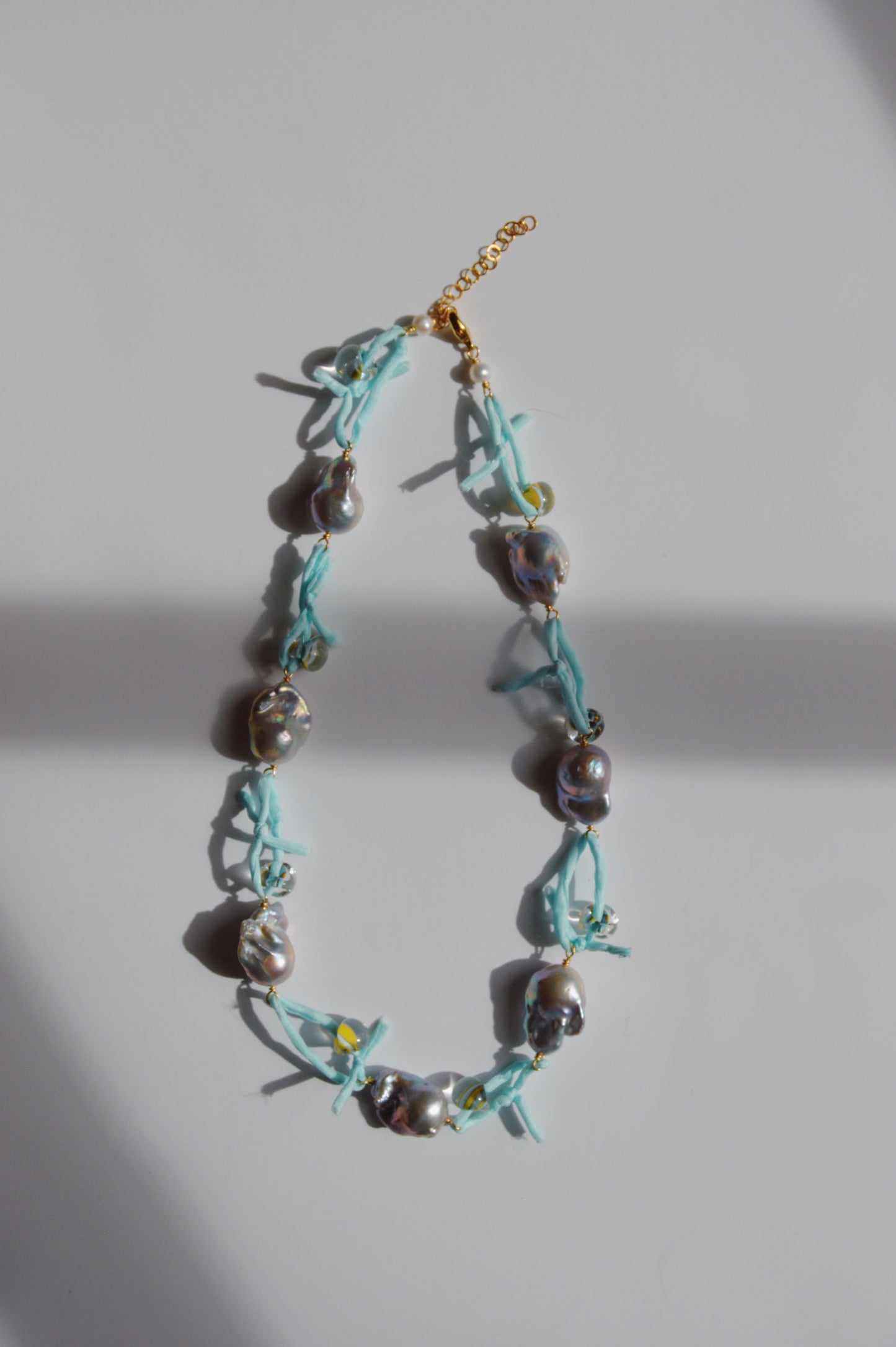 The Silk and Pearl Layer- Robin's Egg features irregular silver freshwater pearls on a light blue silk ribbon with a gold chain clasp, displayed on a white surface with soft shadows—a unique handmade jewelry piece.