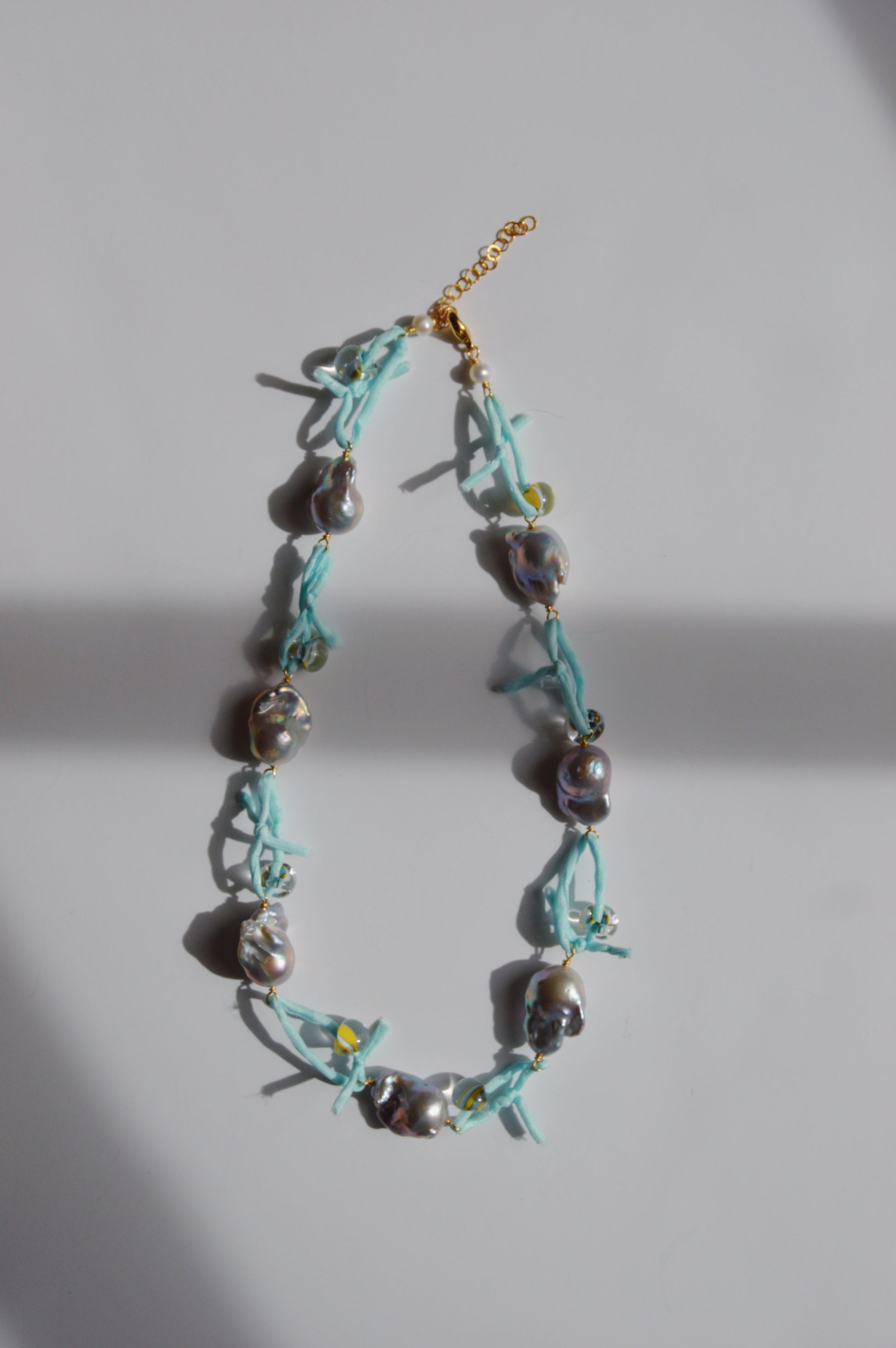 The Silk and Pearl Layer- Robin's Egg features irregular silver freshwater pearls on a light blue silk ribbon with a gold chain clasp, displayed on a white surface with soft shadows—a unique handmade jewelry piece.