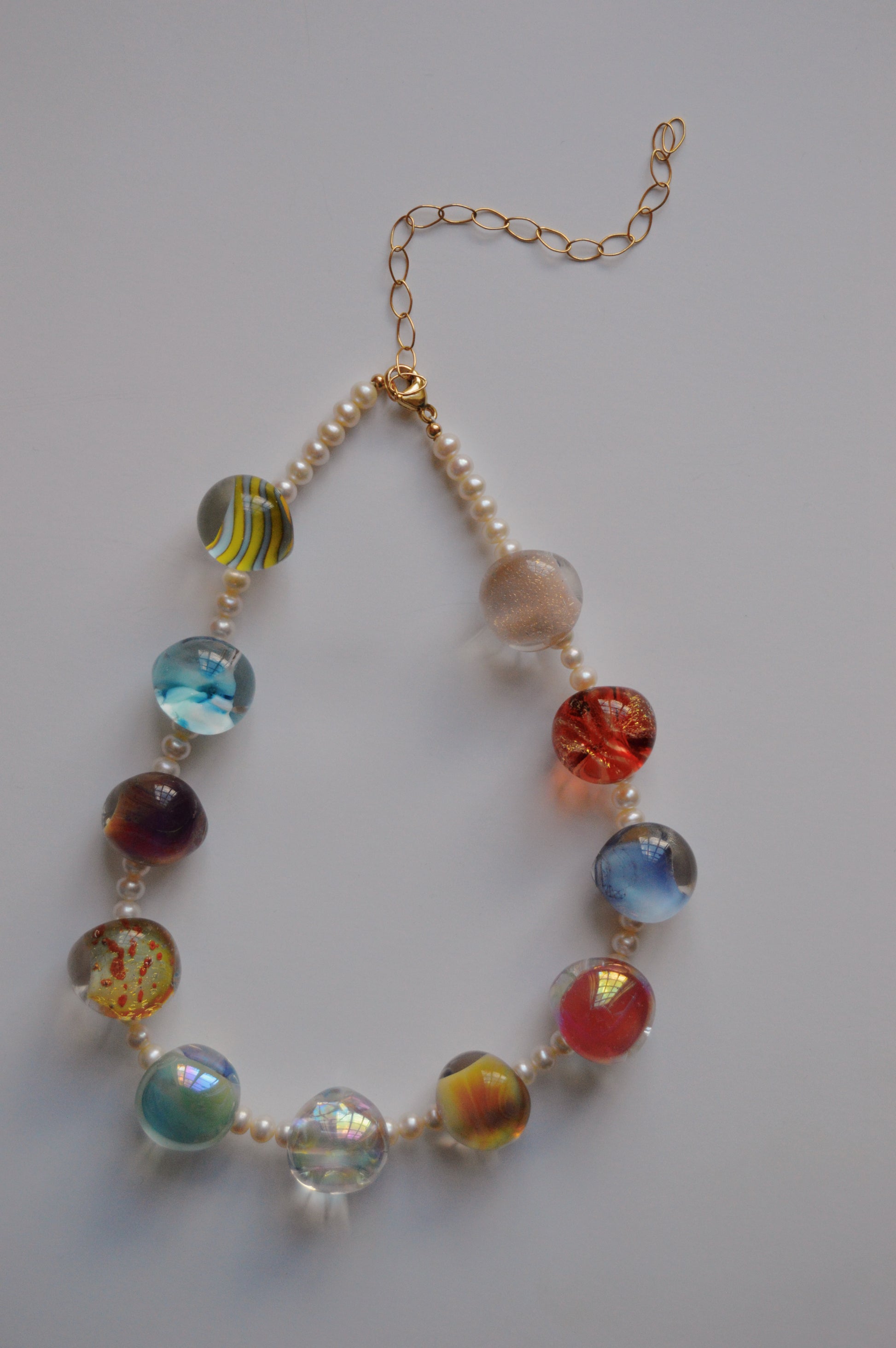 The Grand Bubble and Pearl Layer necklace features alternating handmade lampwork glass beads in various colors and patterns, small freshwater pearls, gold-filled findings, and a gold chain extender, shown on a white background.