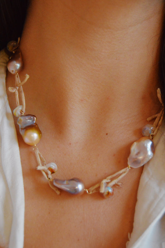 A close-up of a person’s neck wearing the Silk and Pearl Layer- Sandy Puka necklace—handmade with freshwater pearls and twine—paired with a white top.