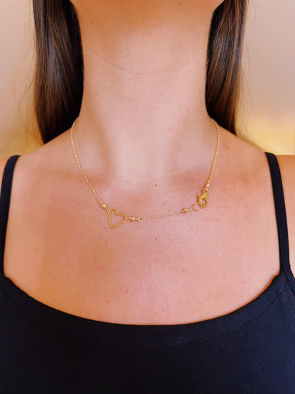 A woman wears the Clasp in Front Layer necklace, featuring a 14K gold filled heart-shaped charm with the letter G on a 16-inch chain, resting at the base of her neck and paired with a classic black tank top.