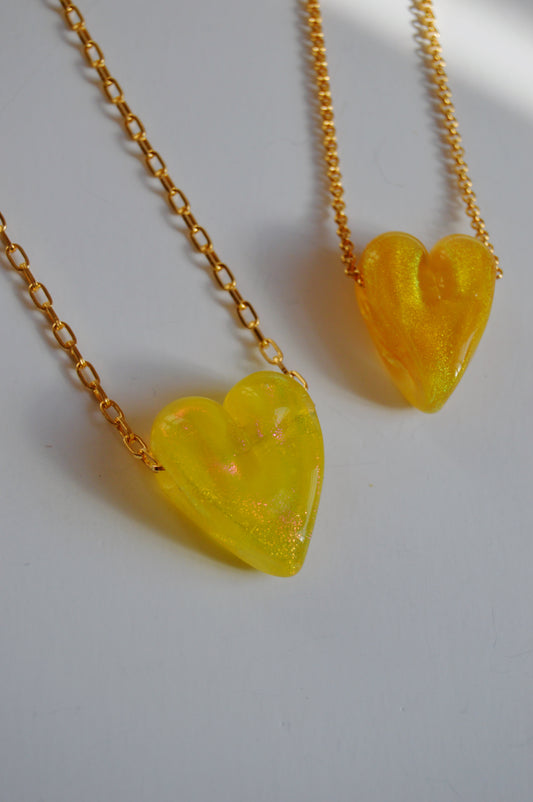 Two Glass Heart Necklaces- Yellows & Golds are displayed on a white surface, featuring gold-filled chains and yellow translucent handmade lampwork glass heart pendants with a shiny, sparkly artisan finish.