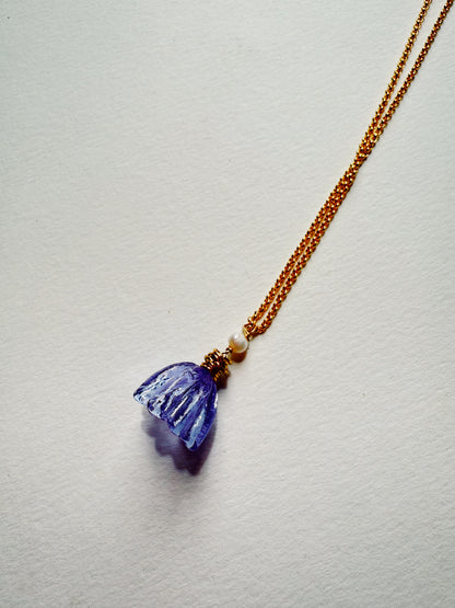 The Tulip Necklace features a 14k gold filled chain with a carved translucent purple stone pendant, accented by a small white bead and gold details, displayed on a white textured background.