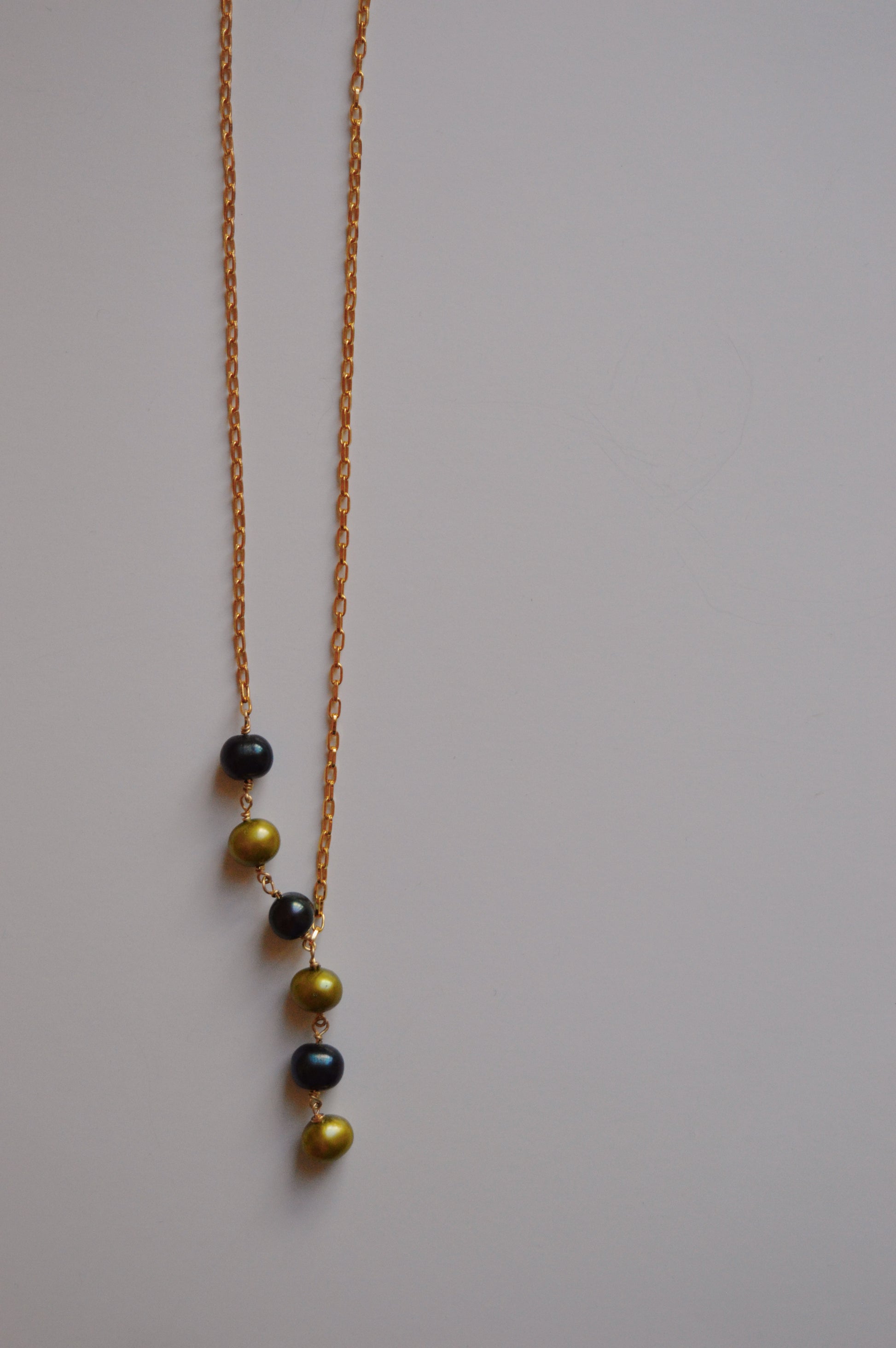 The Six Pearl Lariat—Blue and Green Mix is a handcrafted necklace featuring six alternating blue and green pearls in a vertical line on a 14k gold-filled chain, showcased against a plain light background.