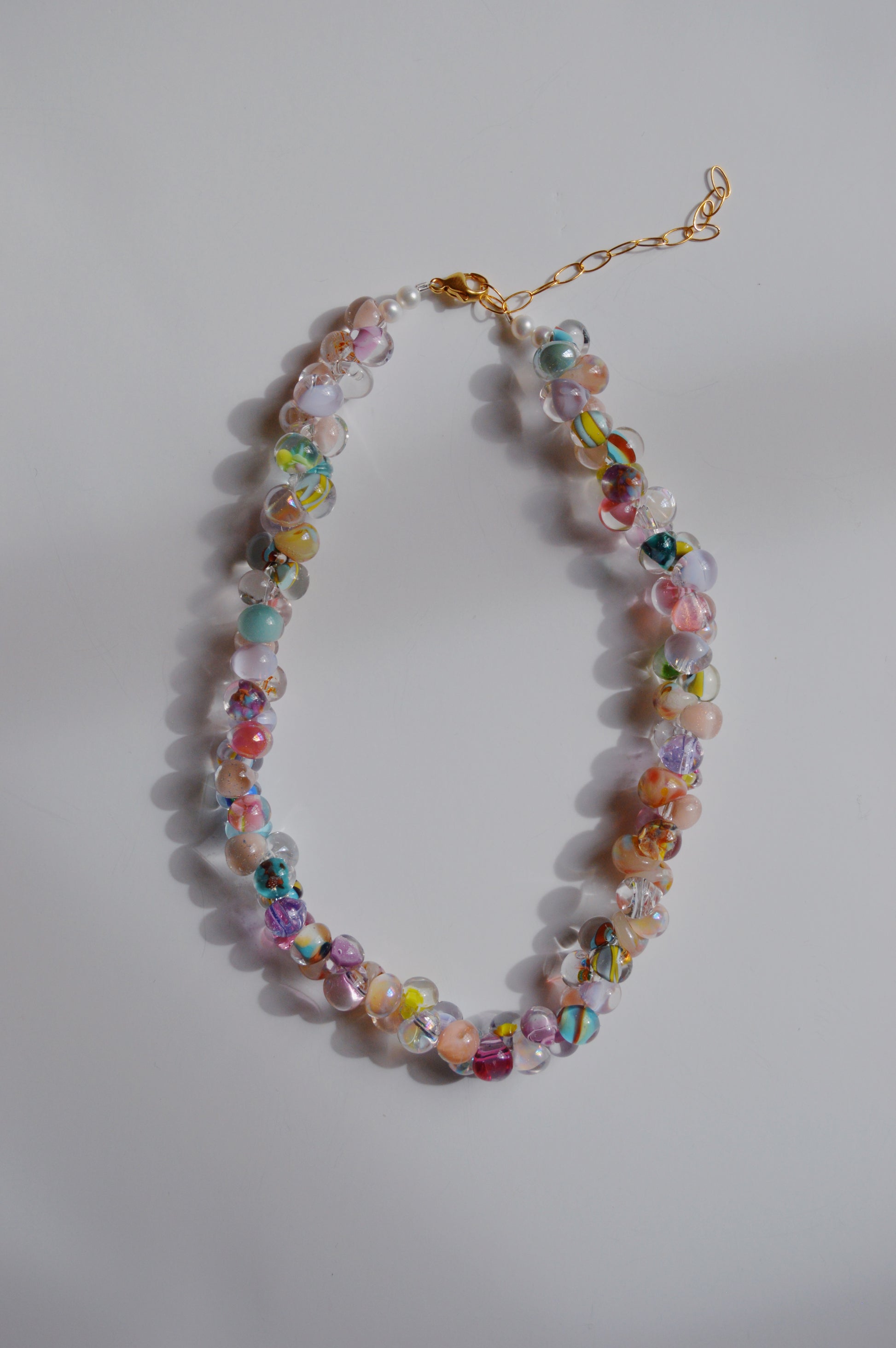 The Rainbow Bubble Glass Necklace in peep color features handmade lampwork glass beads and a gold chain and clasp, displayed in an oval shape on a plain white background.