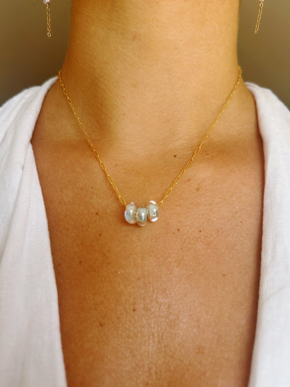 A close-up of a person wearing the Dainty Donut Layer—a 14K gold chain necklace with three irregular pearls—against tan skin and a white top.