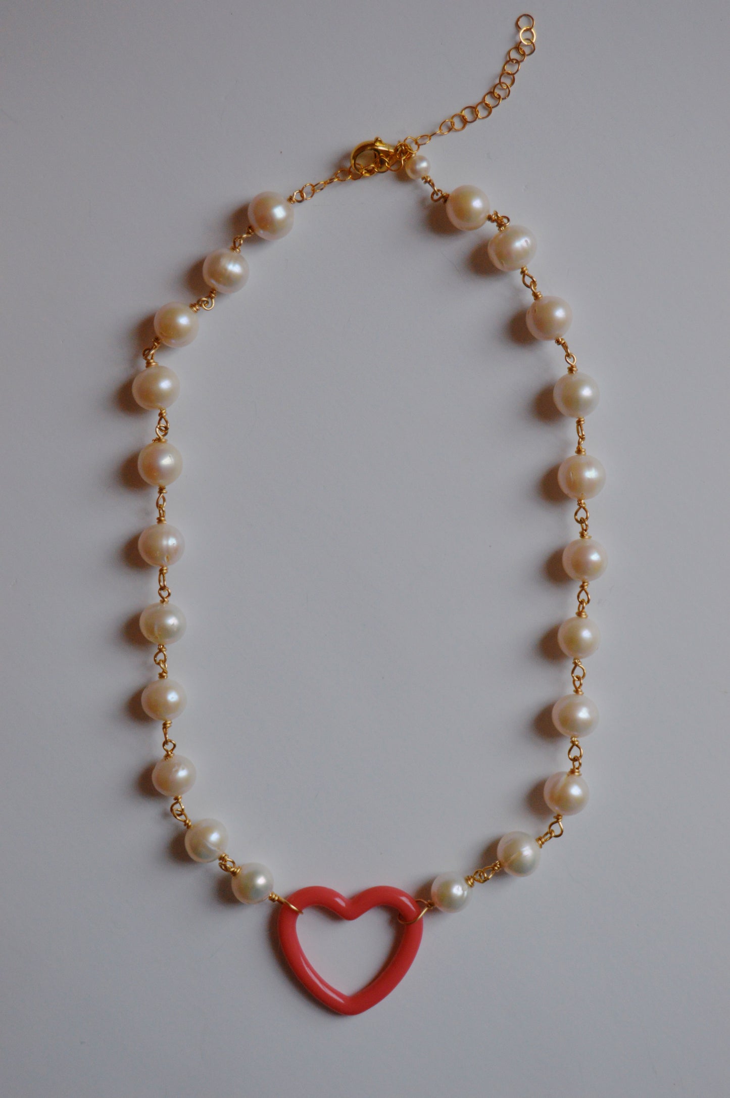 The Open Heart on Pearl Chain features large white freshwater pearls linked with gold-filled findings and clasp, accented by an acrylic heart charm pendant at the center.