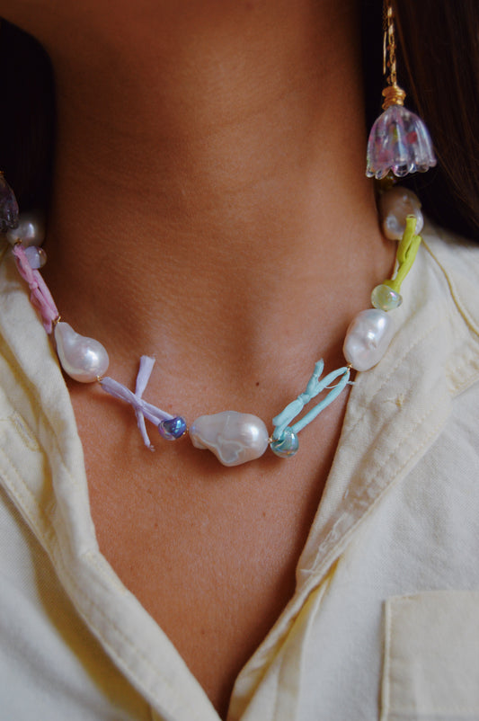 Close-up of a person wearing the Silk and Pearl Layer- Rainbow necklace, featuring handmade freshwater pearls, colorful beads, pastel fabric ties, and a matching earring, styled with a cream collared shirt.