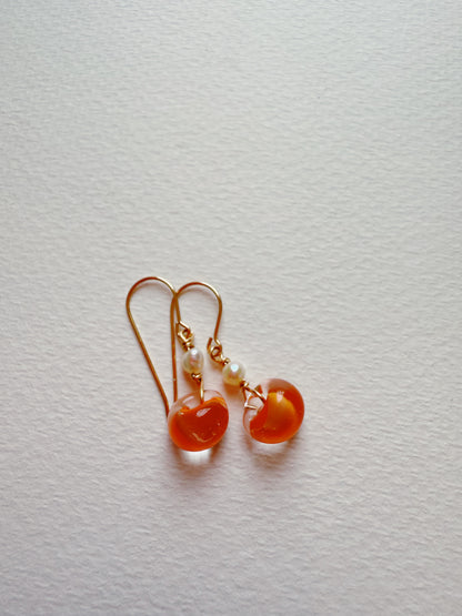Bubble Minis: Gold hook earrings featuring round orange glass beads and delicate freshwater pearl accents, shown on a textured white background.