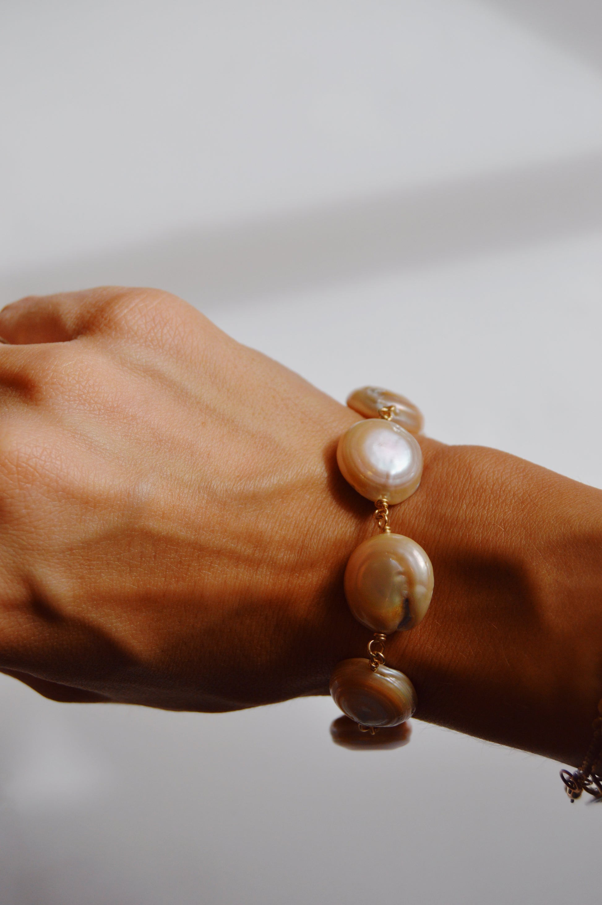 A close-up of a hand wearing the Circle Pearl Bracelet, featuring large round cultured freshwater pearls on a 14k gold-filled chain, set against a softly lit, neutral background.