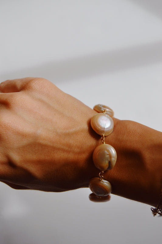 A close-up of a hand wearing the Circle Pearl Bracelet, featuring large round cultured freshwater pearls on a 14k gold-filled chain, set against a softly lit, neutral background.