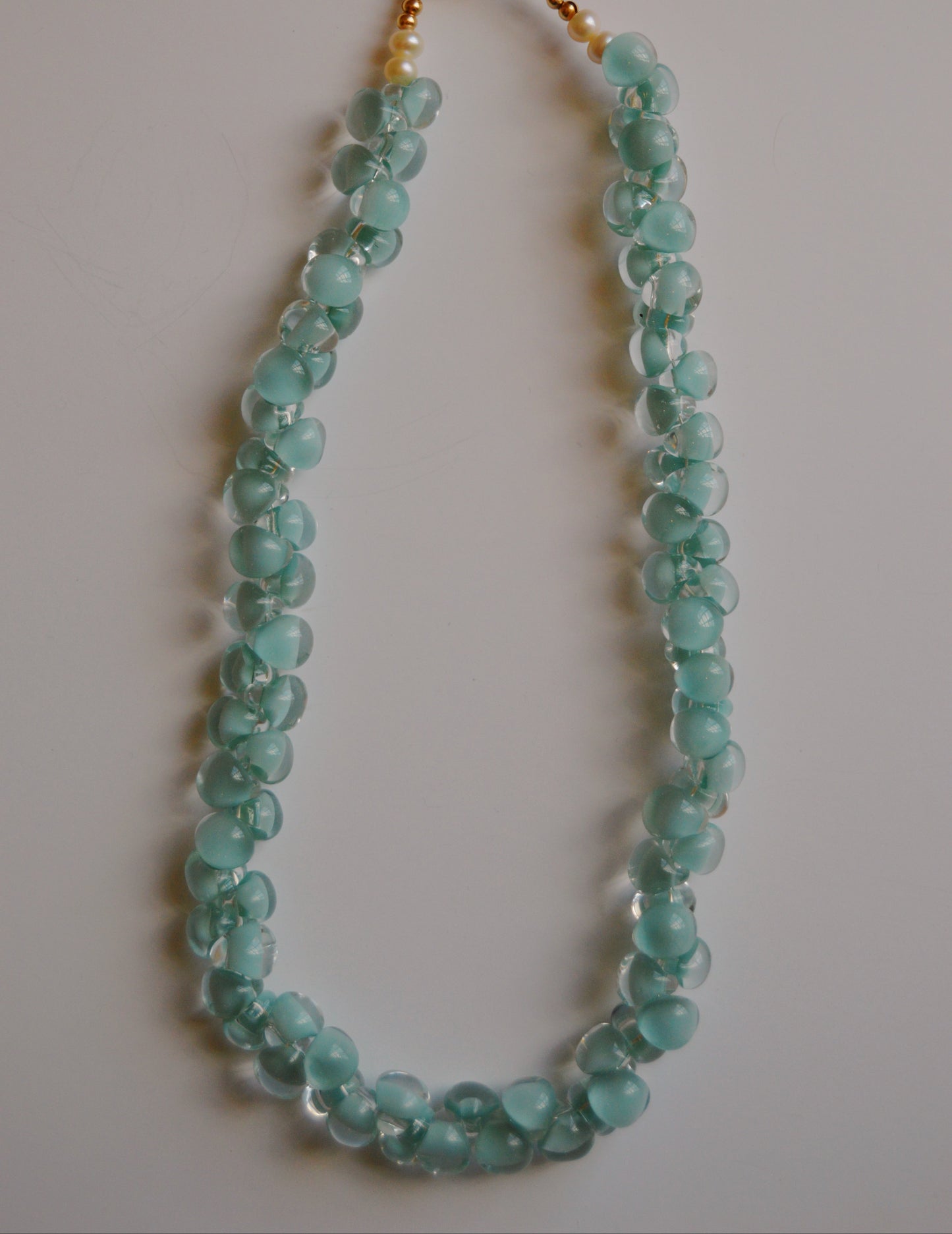 The Bubble Glass Necklace- Santorini features light blue, irregularly shaped handmade lampwork glass beads, a gold clasp, and an adjustable gold chain, shown on a plain white background.