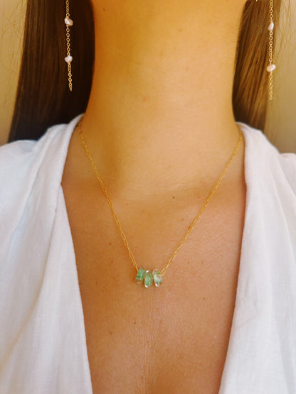 A woman wearing the Dainty Donut Layer—a 14K gold chain necklace with three green beads—and matching gold chain earrings with small pearls, styled with a white v-neck top.