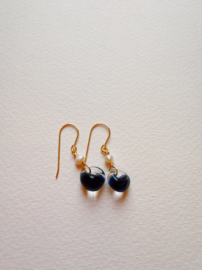 Bubble Minis are gold hook earrings with gold-filled findings, small white beads, and round dark blue glass pendants, shown on a textured white surface.