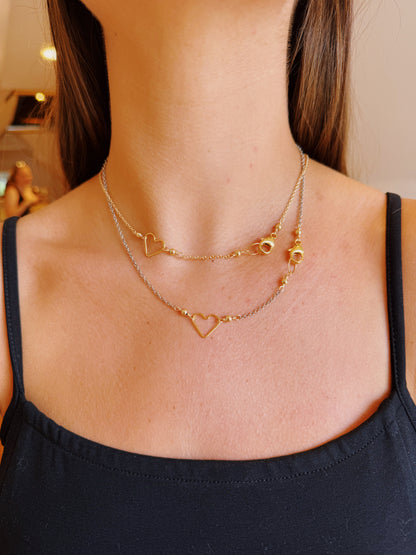 A woman wearing a black top showcases the Clasp in Front Layer: two delicate gold chains, featuring a 14K gold filled heart pendant and an oxidized sterling silver chain, elegantly layered around her neck.