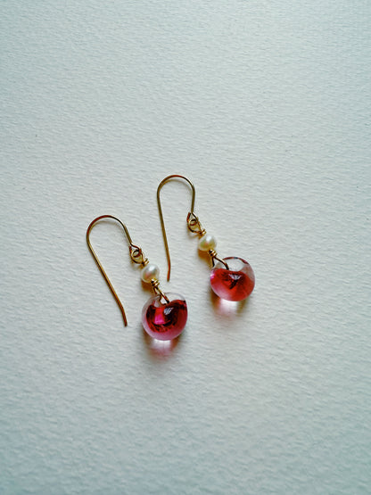 The Bubble Minis are gold hook earrings with gold-filled findings, small freshwater pearls, and translucent pink teardrop charms, shown on a textured white background.